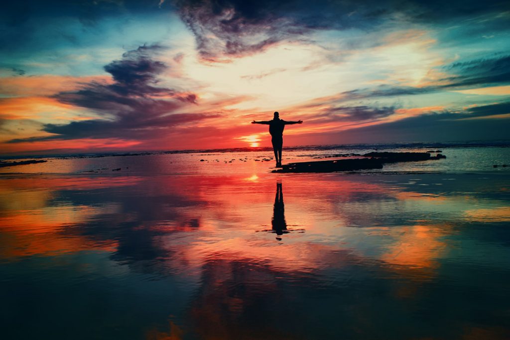 Silhouette of person with arms open to a sunset or sunrise.