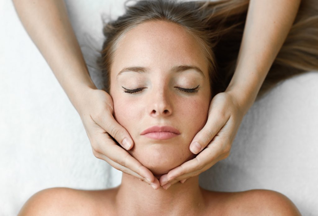 Women with eyes closed lying down with hands wrapped around her face.