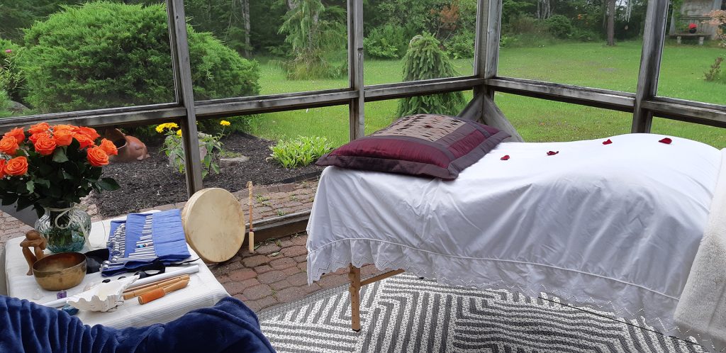 Screened in space with massage table, flowers and sound healing tools.