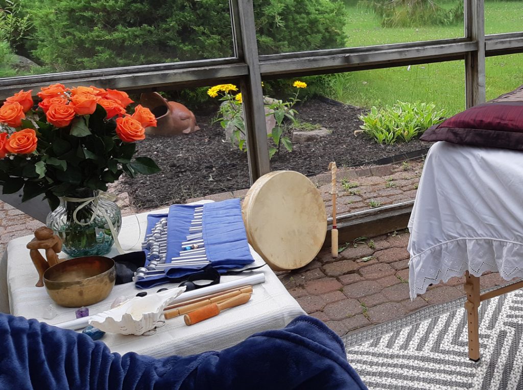 Table with sound healing tools, crystals and vase filled with roses.