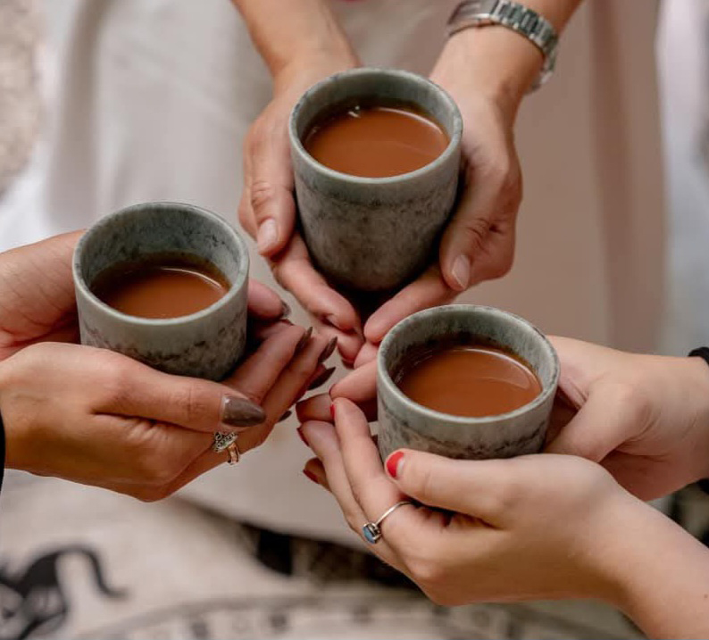 Three hands holding cacao in mugs.